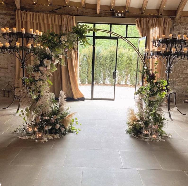 Decorative floral arches with candles in a room with large windows and stone walls.