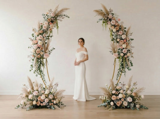 Woman in a white wedding dress standing between two floral arches with pink and green flowers.